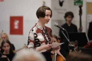 Slavnostna gostja ob mikrofonu nagovarja obiskovalce 20. Obletnice Rastoče knjige.