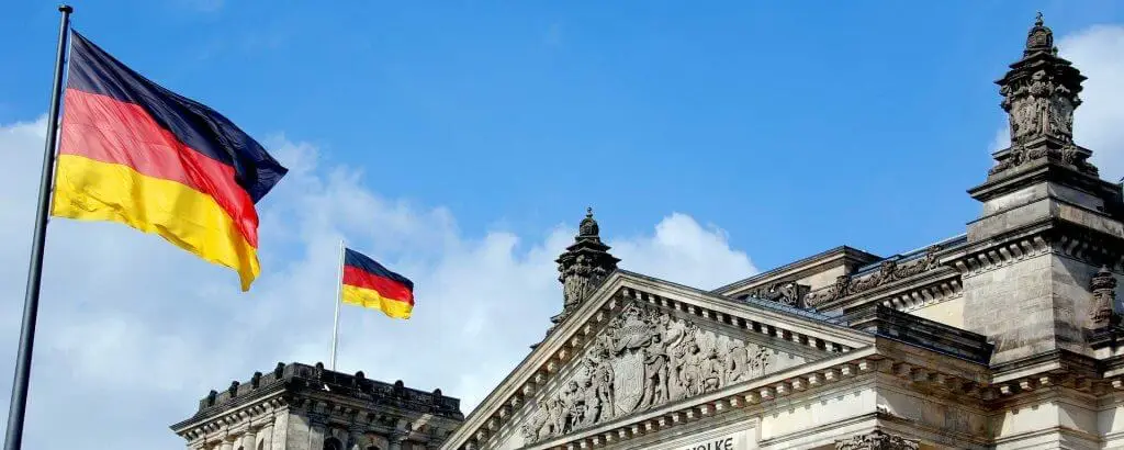 Nemška zastava plapola na oblačnem nebu, v ozadju vrh stavbe Reichstag v Berlinu.