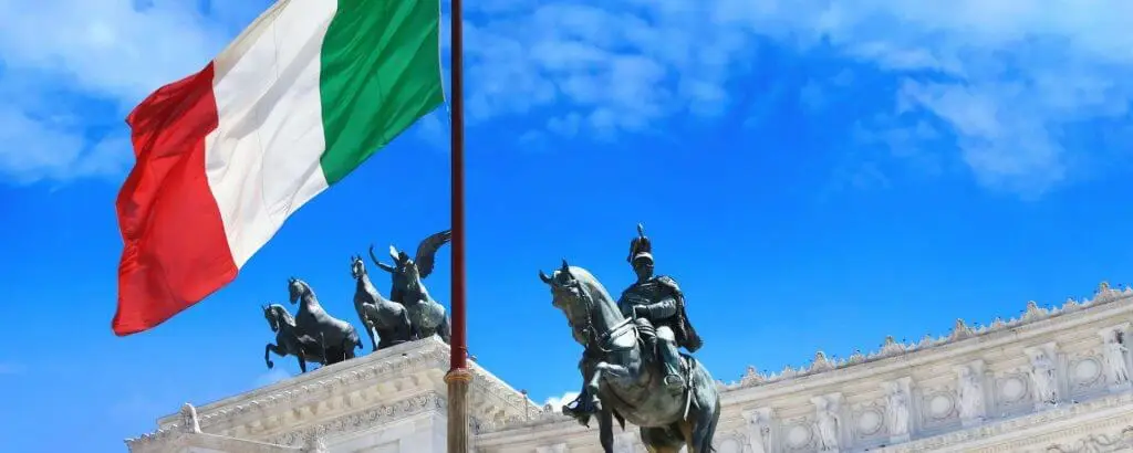 Italijanska zastava plapola pod modrim nebom, v ozadju kipi konjenice.