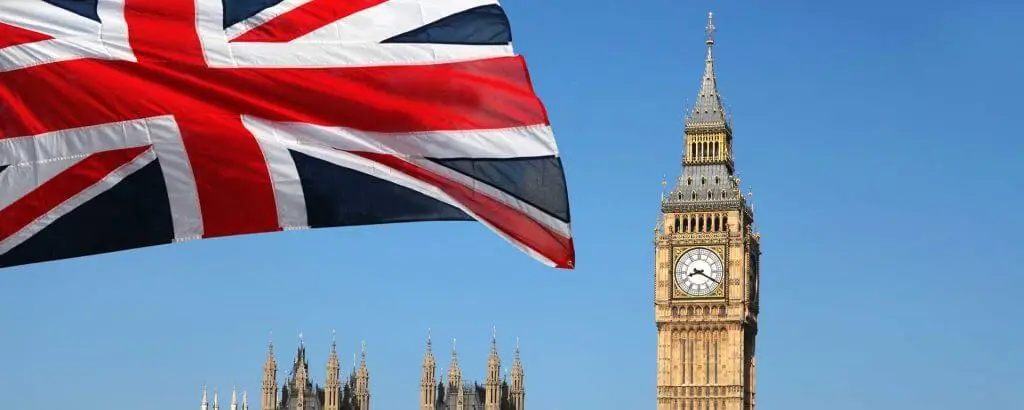 Zastava Velike Britanije plapola na modrem nebu, v ozadju zvonik Big Bena.